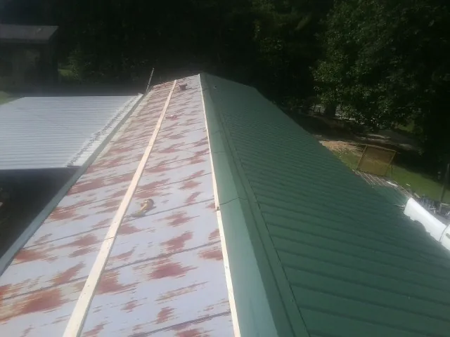 Old rusted panels beside newly installed green metal roofing — Wind Damage Roof Repair by Roofing Brothers in Taylor Ridge
