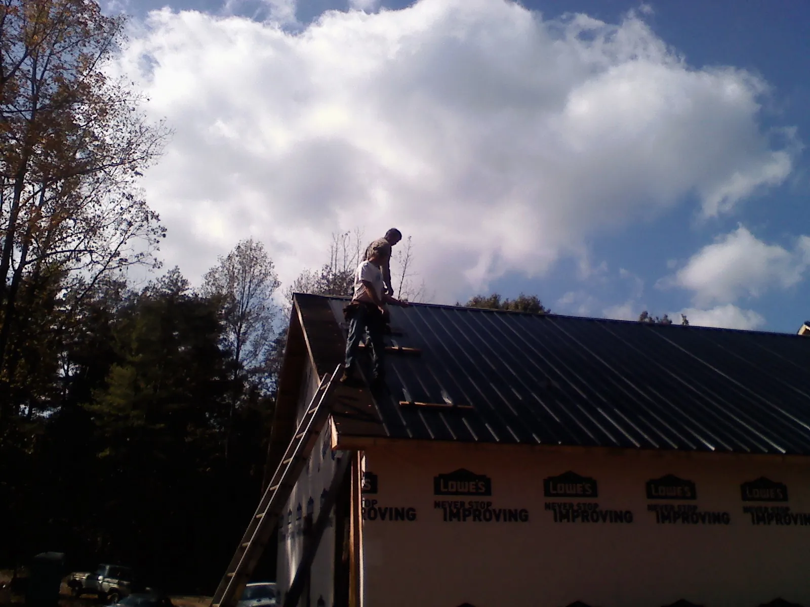 Roofer fastening dark metal panels high against a cloudy sky, from a Roof Inspection job in Taylor Ridge