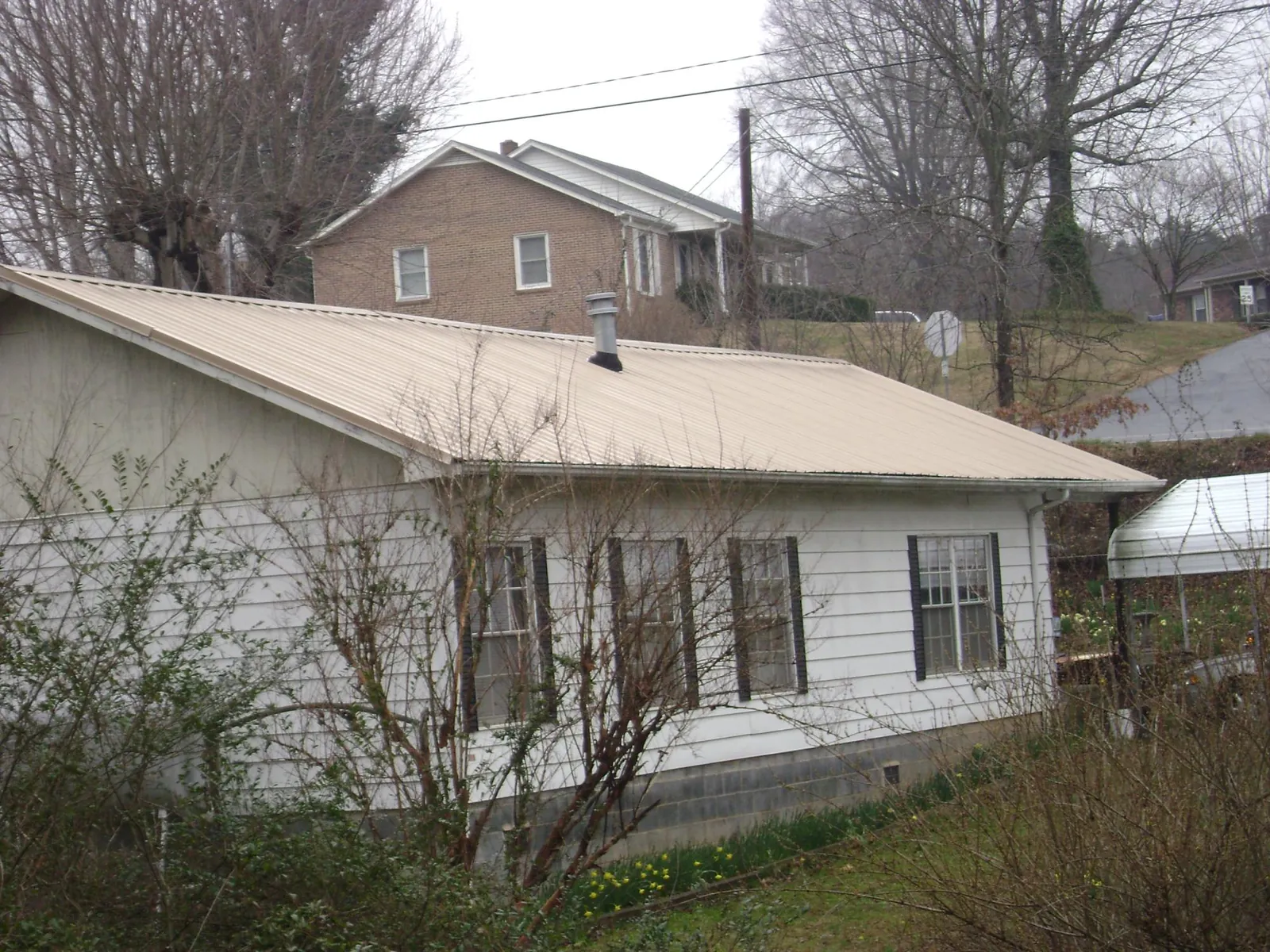 Tan metal roof on a white sided house set into a hillside — Commercial Roofing by Roofing Brothers in Taylor Ridge